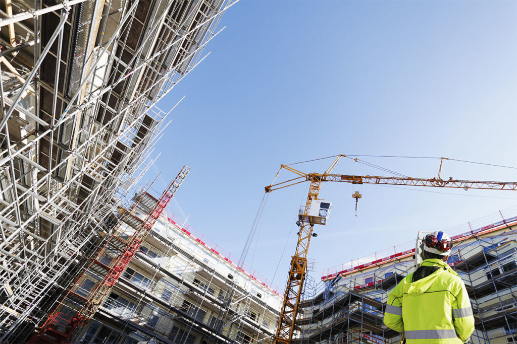 Building works, man in high vis jacket standing under a crane