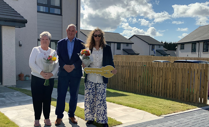 Housing Minister Paul McLennan and two tenants along with a photo of the development