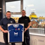 Montrose Port Authority hits major net zero milestone MPA Harbour Master, Ross Marshall, gifting Brage Viking Captain, Jan Pedersen, a Montrose FC t-shirt with proceeds going to PoppyScotland to mark the 1GWh milestone