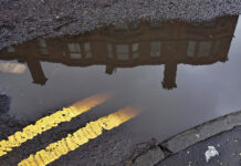 A tenement in a Glasgow street reflected in a puddle with double yellow lines on the road