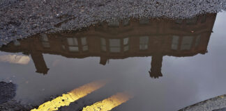 A tenement in a Glasgow street reflected in a puddle with double yellow lines on the road