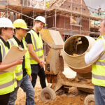 Builder using cement mixer on site with apprentices
