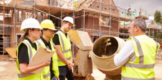 Builder using cement mixer on site with apprentices