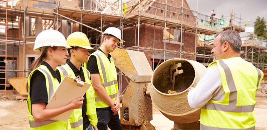 Builder using cement mixer on site with apprentices